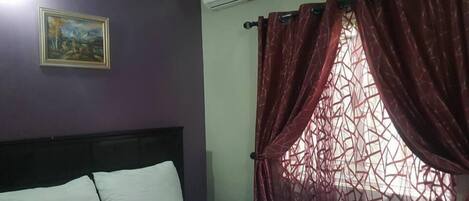Una habitación con una cama, un cuadro en la pared y una ventana con cortinas rojas.