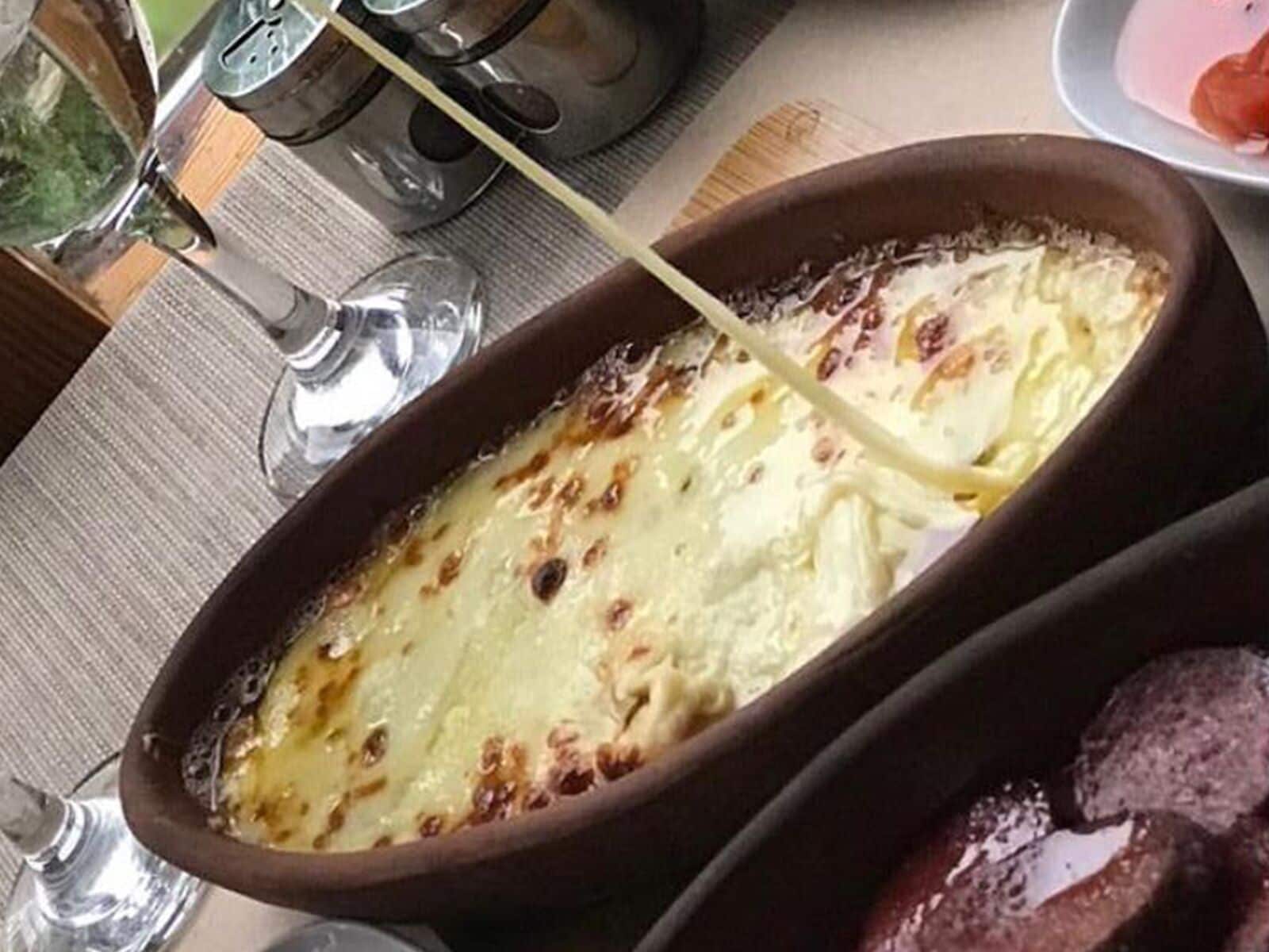 A dish in a ceramic dish with melted cheese on top, a glass of water, and a salt shaker on the table.