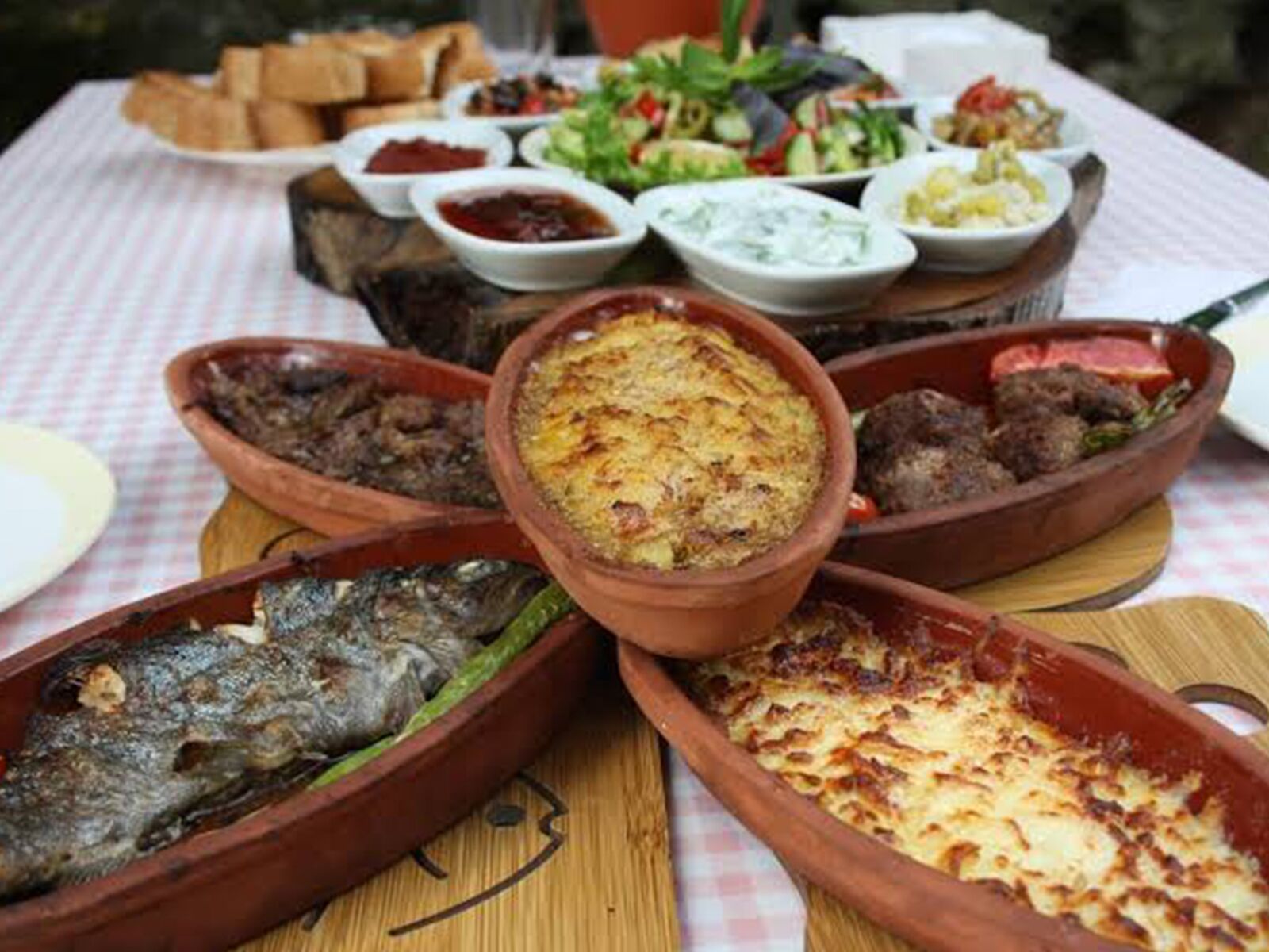 Een tafel met diverse gerechten in terracotta potten, waaronder vis, vlees en een gebakken ovenschotel.