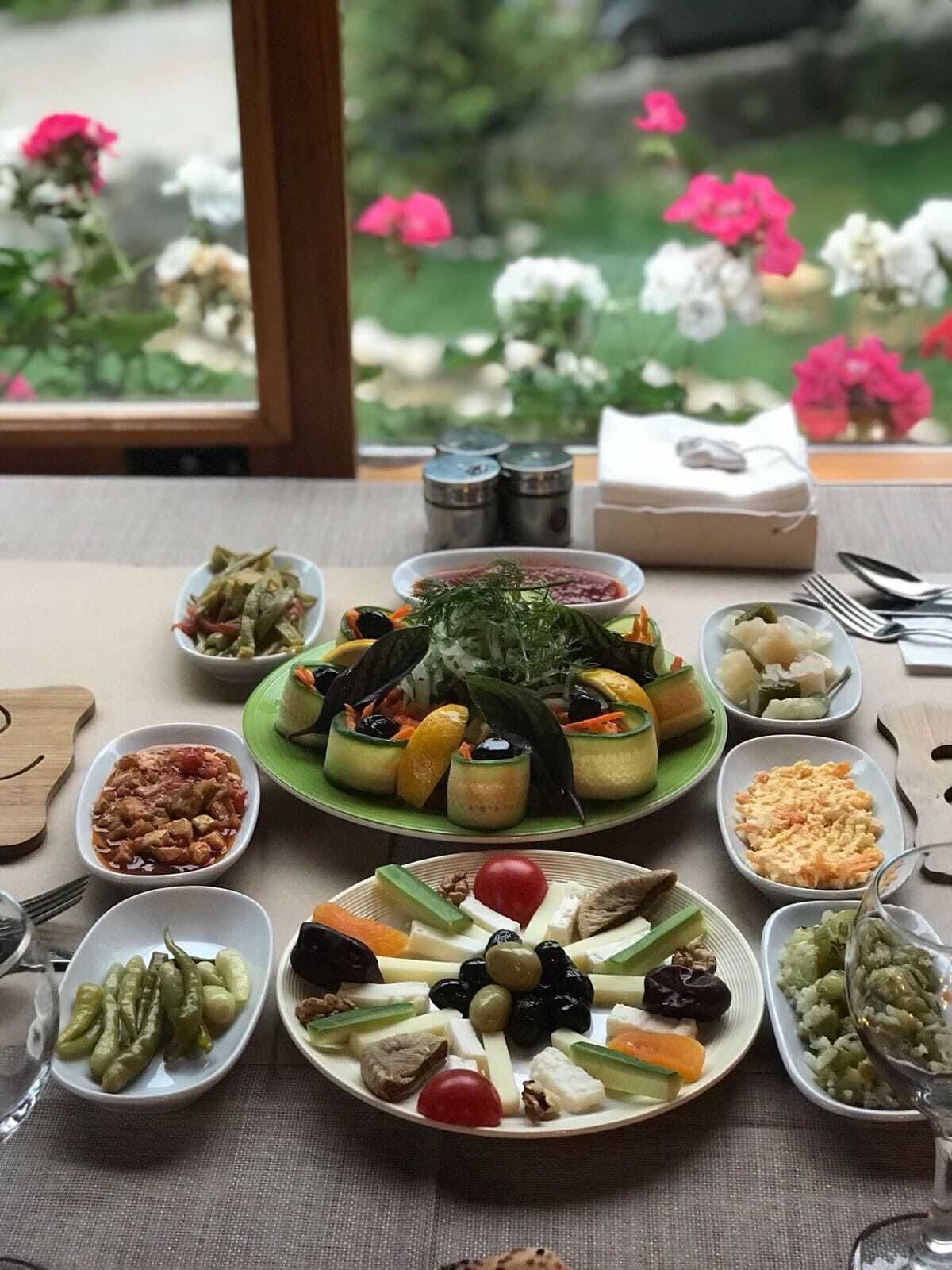 Una mesa dispuesta con diversos platos, como ensaladas, quesos y salsas, con vistas a flores en el exterior.