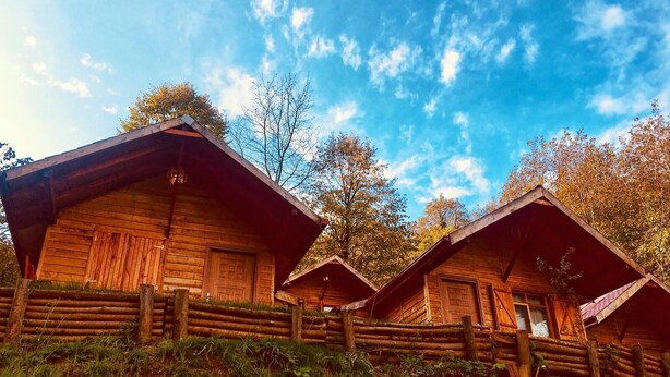 A row of wooden cabins with a sloped roof, surrounded by a wooden fence and greenery. - Yesil Dus Vadisi Bungalow Restoran (Kartepe)
