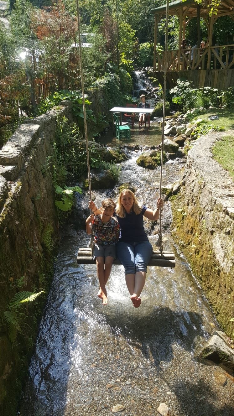 Un stretto canale d'acqua con un ponte basculante in legno, circondato da vegetazione rigogliosa e una piccola cascata.