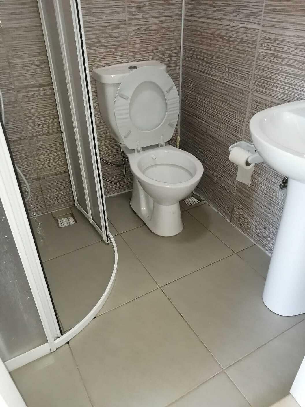Un baño con inodoro, lavamanos y zona de ducha, con piso de baldosas.