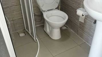 Un baño con inodoro, lavamanos y zona de ducha, con piso de baldosas.