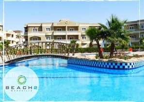 Una piscina con borde a cuadros, rodeada por una palmera y un edificio con balcones.