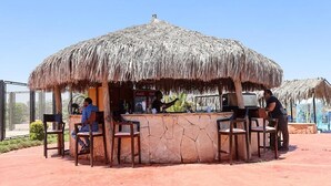 Zona de bar al aire libre con techo de paja, asientos de piedra y una parrilla.