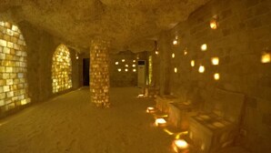 Un interior tenuemente iluminado con paredes de piedra, un pilar central y varias fuentes de luz.