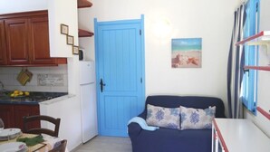Une cuisine compacte avec des meubles en bois, une porte bleue et un coin repas avec une table dressée pour deux personnes.