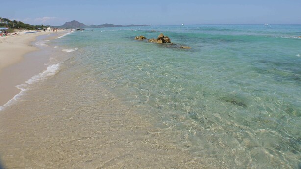Une plage à l’eau turquoise et limpide, avec un rivage sablonneux et des affleurements rocheux.