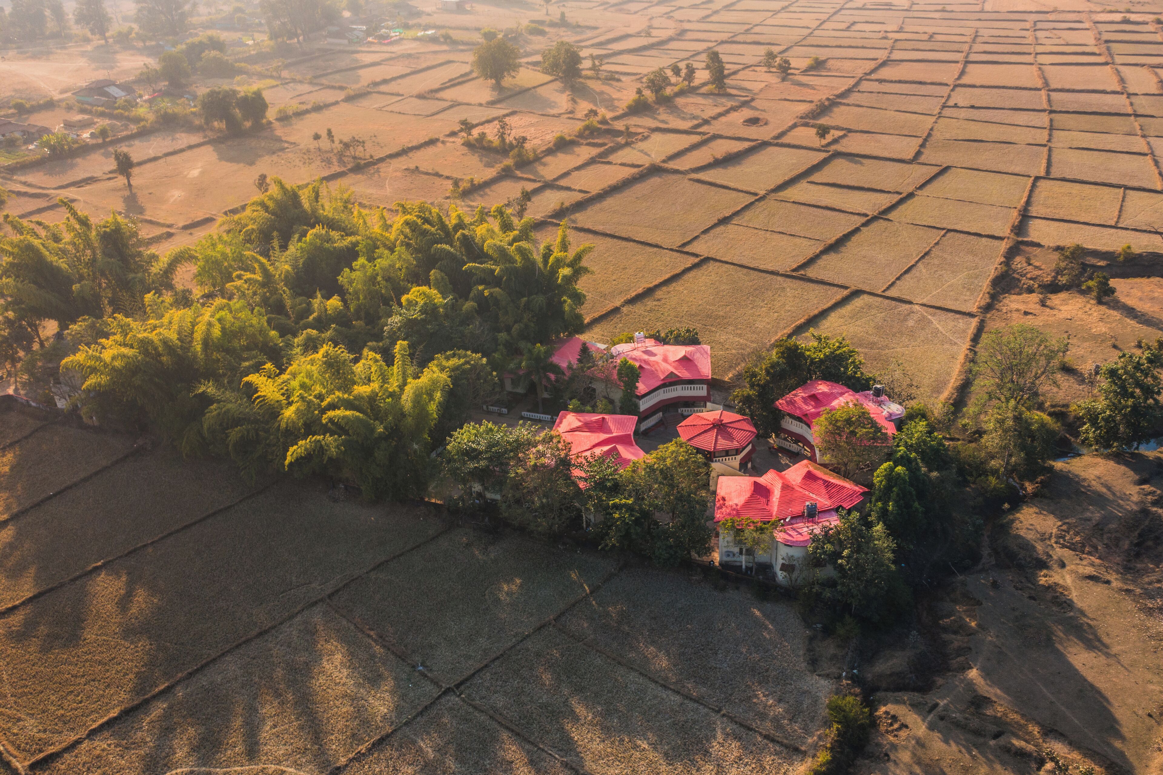 An aerial view of a rural area with fields and a cluster of buildings with red roofs.