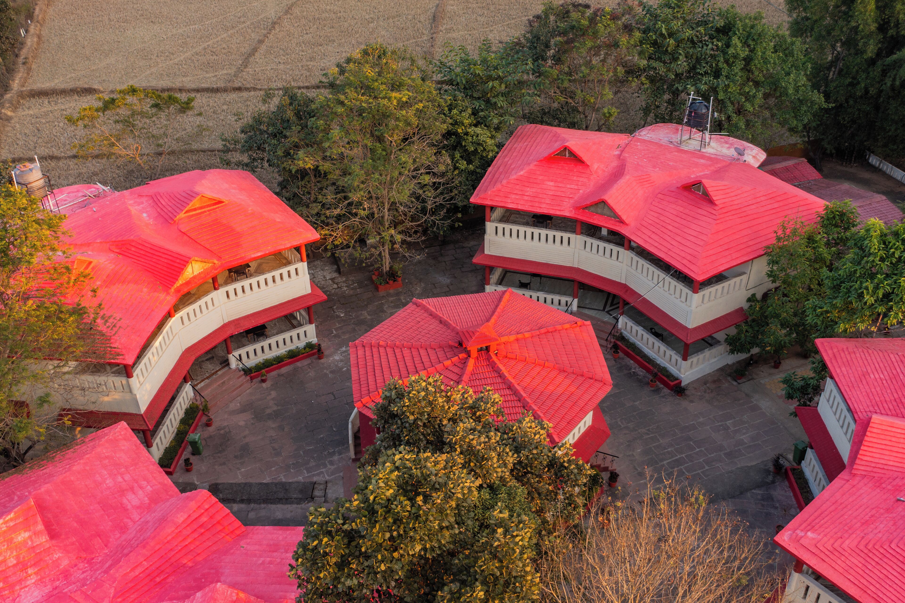 Un ensemble de bâtiments aux toits rouges et aux balcons blancs, entourés d’arbres et d’une zone pavée.