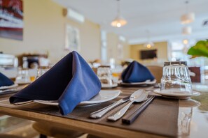 A dining table set with blue napkins, plates, cutlery, and a glass. - Calao Kep Residence Hotel (Kep)