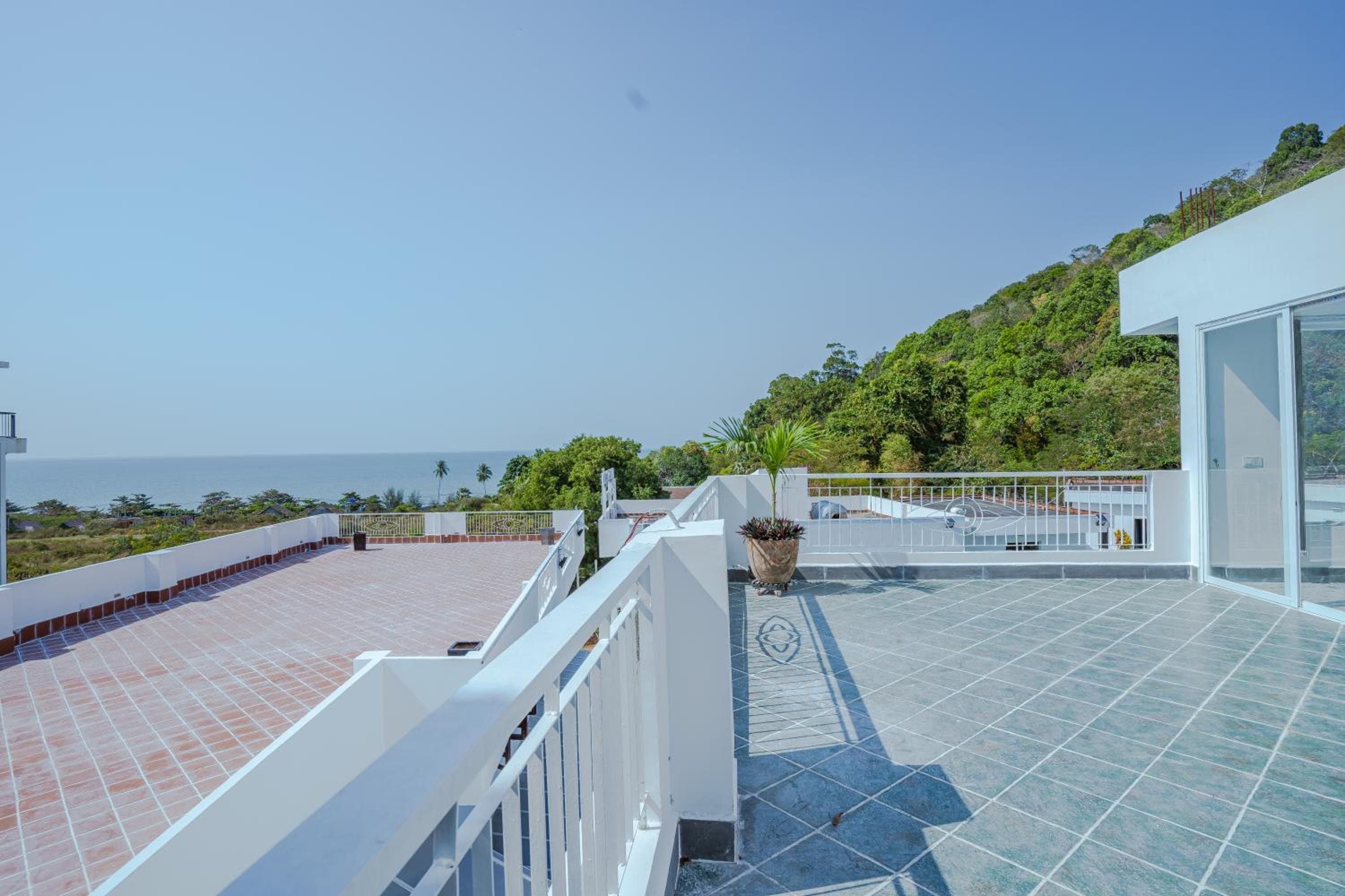 Une terrasse sur le toit offrant une vue sur la mer, un bâtiment blanc et une colline verdoyante.