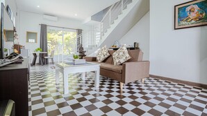A modern living room with a checkered floor, a sofa with patterned cushions, a coffee table, and a staircase. - Calao Kep Residence Hotel (Kep)