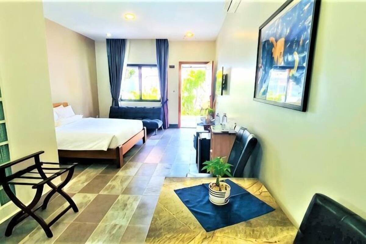 A hotel room with a bed, a desk, a chair, a potted plant, and a view of the outdoors.