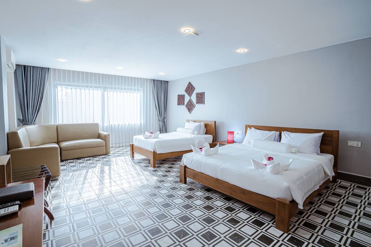 A hotel room with a large bed, two smaller beds, a sofa, and a desk with a chair.