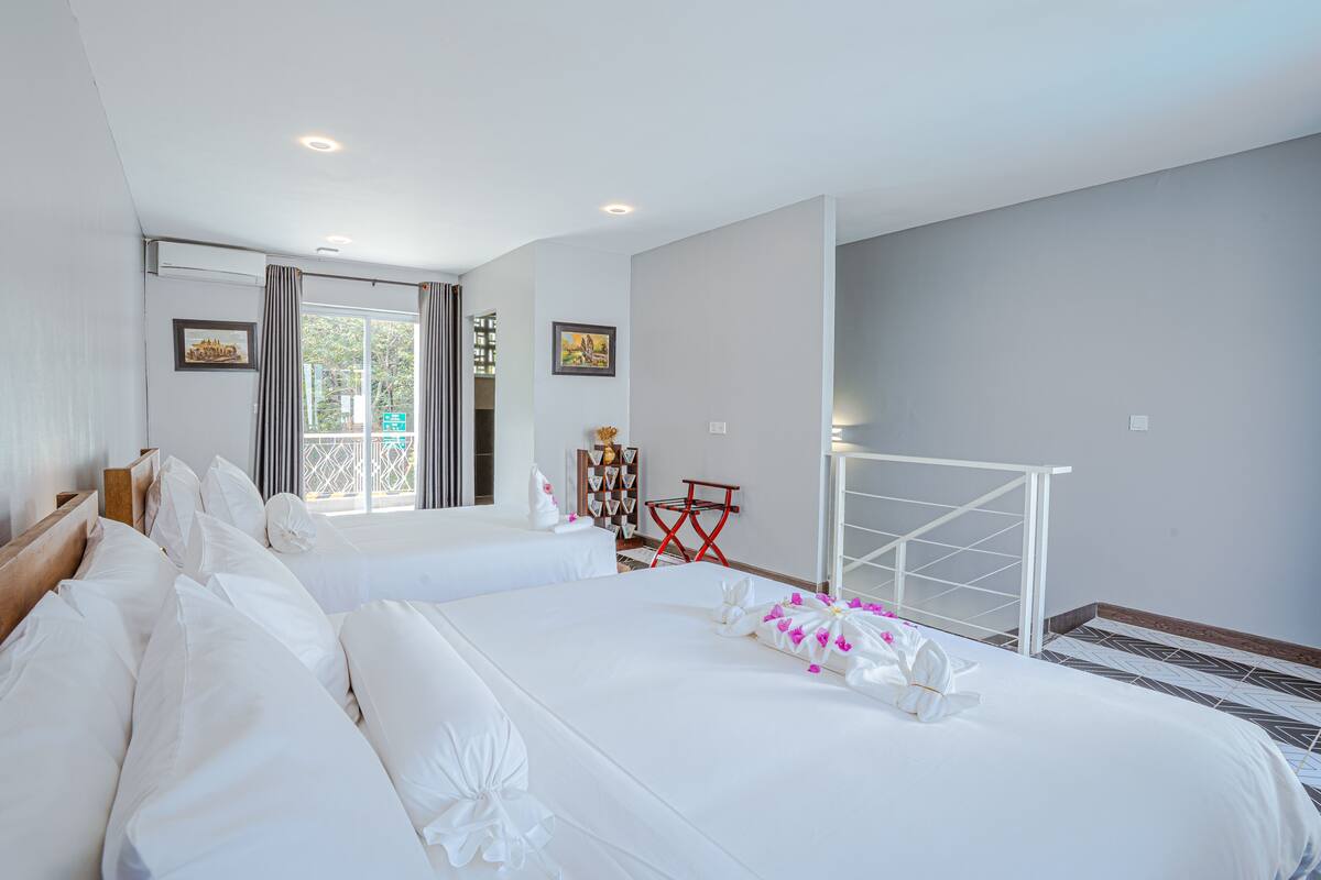 A hotel room with two beds, a window with curtains, a red chair, a white metal bed frame, and a view of greenery outside.