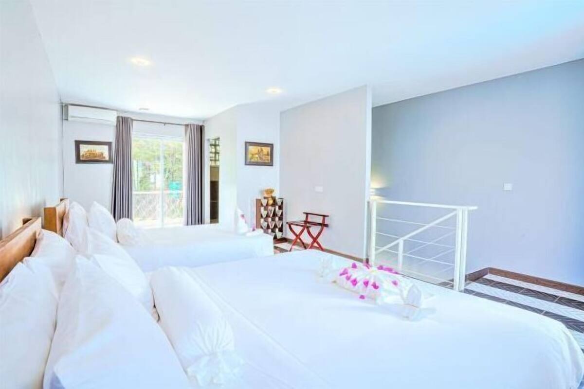 A hotel room with two beds, a window with curtains, a small table, and a chair.