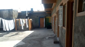 Une cour avec un sol en béton, un étendoir à linge où sont suspendus des vêtements blancs, et un bâtiment doté d’une porte et de fenêtres en bois.