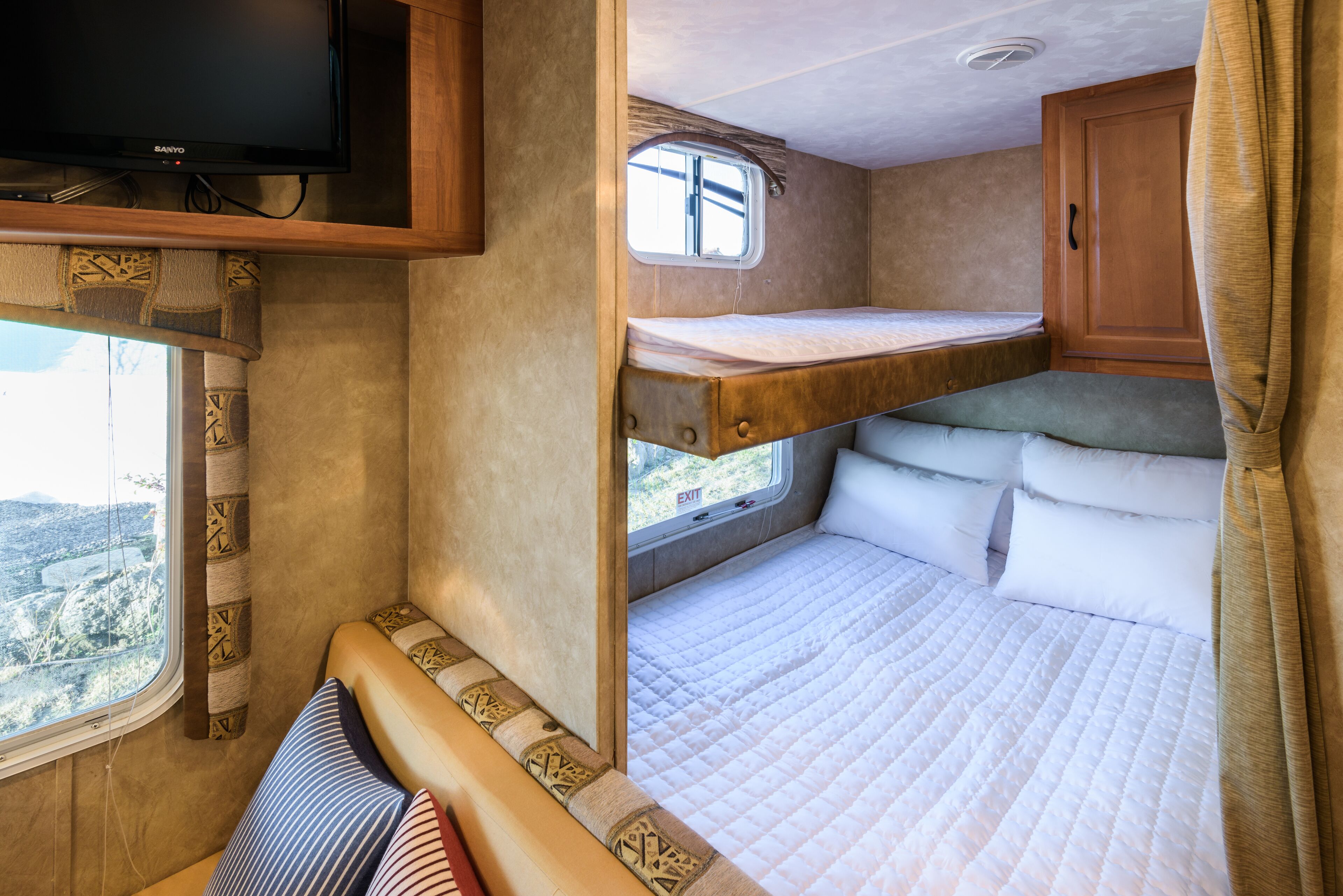 Un intérieur de camping-car compact comprenant un lit superposé, un téléviseur fixé au-dessus du lit et une fenêtre donnant sur l’extérieur.