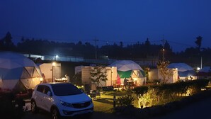 Eine Reihe von kuppelartigen Zelten mit angebauten Kabinen, ein weißes Auto davor, und eine kleine Sitzgelegenheit im Freien mit Tischen und Stühlen.