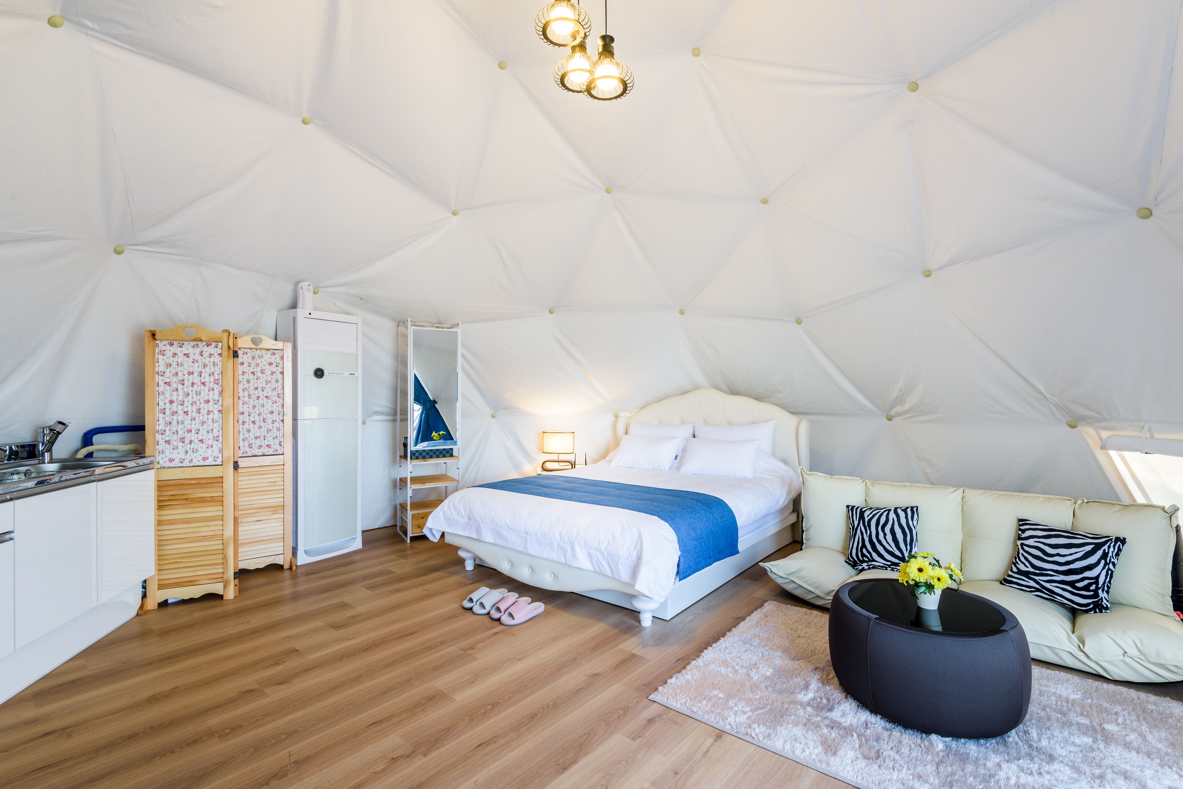 A tented accommodation with a bed, sofa, and a small kitchen area.