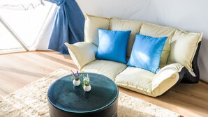 Ein gemütliches Wohnzimmer mit einer Couch, einem runden Hocker und einem kleinen Tisch mit Topfpflanzen.