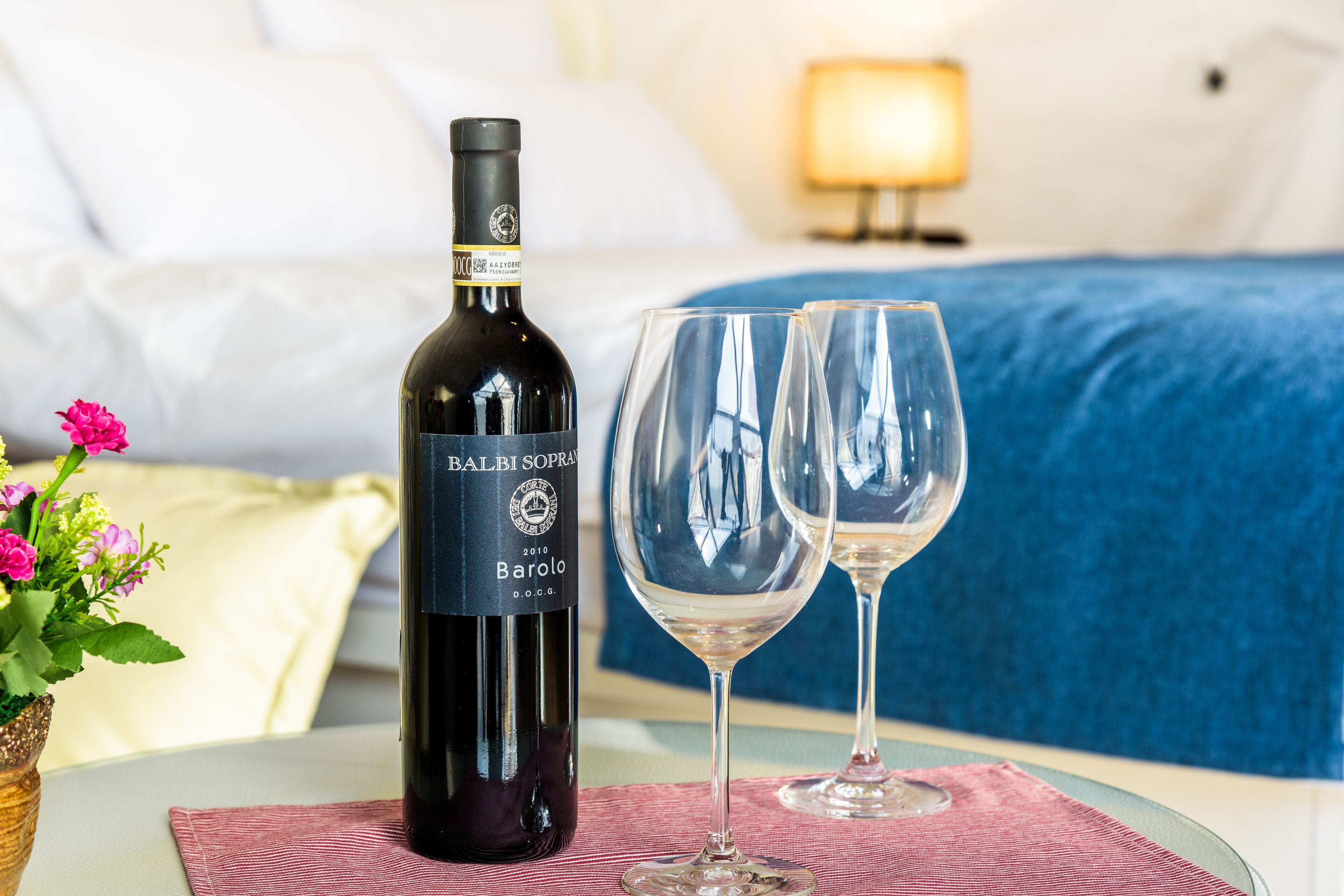 Una botella de vino Barolo y dos copas de vino sobre una mesa en una habitación de hotel.