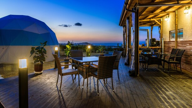 Eine Holzterrasse mit Gartenmöbeln, ein überdachter Bereich mit Tisch und Stühlen und Blick auf den Ozean bei Dämmerung.