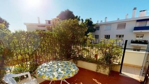 Une terrasse avec une table ronde et des chaises, entourée de plantes et d’une clôture.