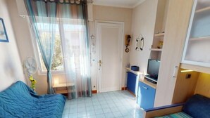 Une chambre de taille modeste, équipée de deux lits, d’un petit bureau, d’une télévision et d’une fenêtre avec des rideaux.