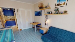 Une pièce de taille modeste, avec un canapé bleu, un petit bureau et une kitchenette dotée de meubles bleus.