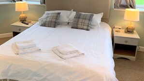 Ein ordentlich bezogenes Bett mit weißen Laken und zwei Kissen, eine Nachttischlampe und ein kleiner Nachttisch mit Lampe.