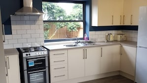 Eine moderne Küche mit weißen Schränken, einem Edelstahl-Dunstabzug, einem eingebauten Backofen und einem Fenster mit Blick auf Grünfläche.