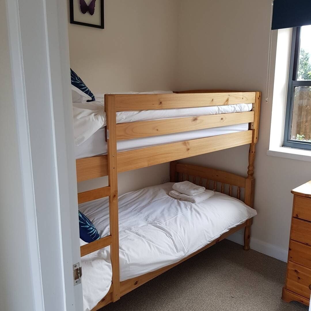 A bunk bed with white bedding, a wooden headboard, and a window with a view of greenery.