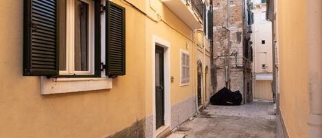 Un callejón estrecho con un edificio que tiene una puerta y ventanas con contraventanas.
