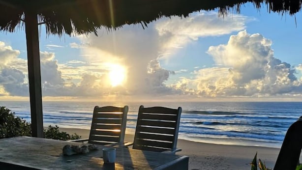 A beachside table with two chairs under a thatched roof, overlooking the ocean with a sunset. - Aloha 1 (Ponta d'Ouro)