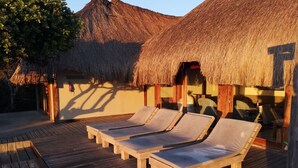 A wooden deck with lounge chairs and a pool, surrounded by thatched-roof structures. - Aloha 1 (Ponta d'Ouro)