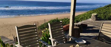 A table with chairs and plates, overlooking a beach with waves.