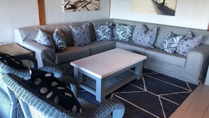 A cozy living area with a grey sofa, patterned cushions, a white coffee table, and a woven chair. - Aloha 1 (Ponta d'Ouro)
