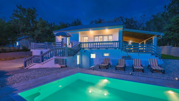 Ein zweigeschossiges Haus mit Swimmingpool, einer überdachten Terrasse mit Liegestühlen und einer Treppe, die zum Obergeschoss führt.