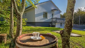 Ein Holzbottich mit einer Tasse und einem Untertasse auf einer grasbewachsenen Fläche, umgeben von Bäumen, mit einem Haus im Hintergrund.