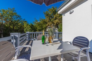 Une terrasse avec une table blanche, deux chaises, une bouteille de champagne et un ananas.