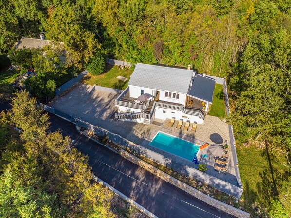 Une grande maison avec une piscine, entourée d’arbres.