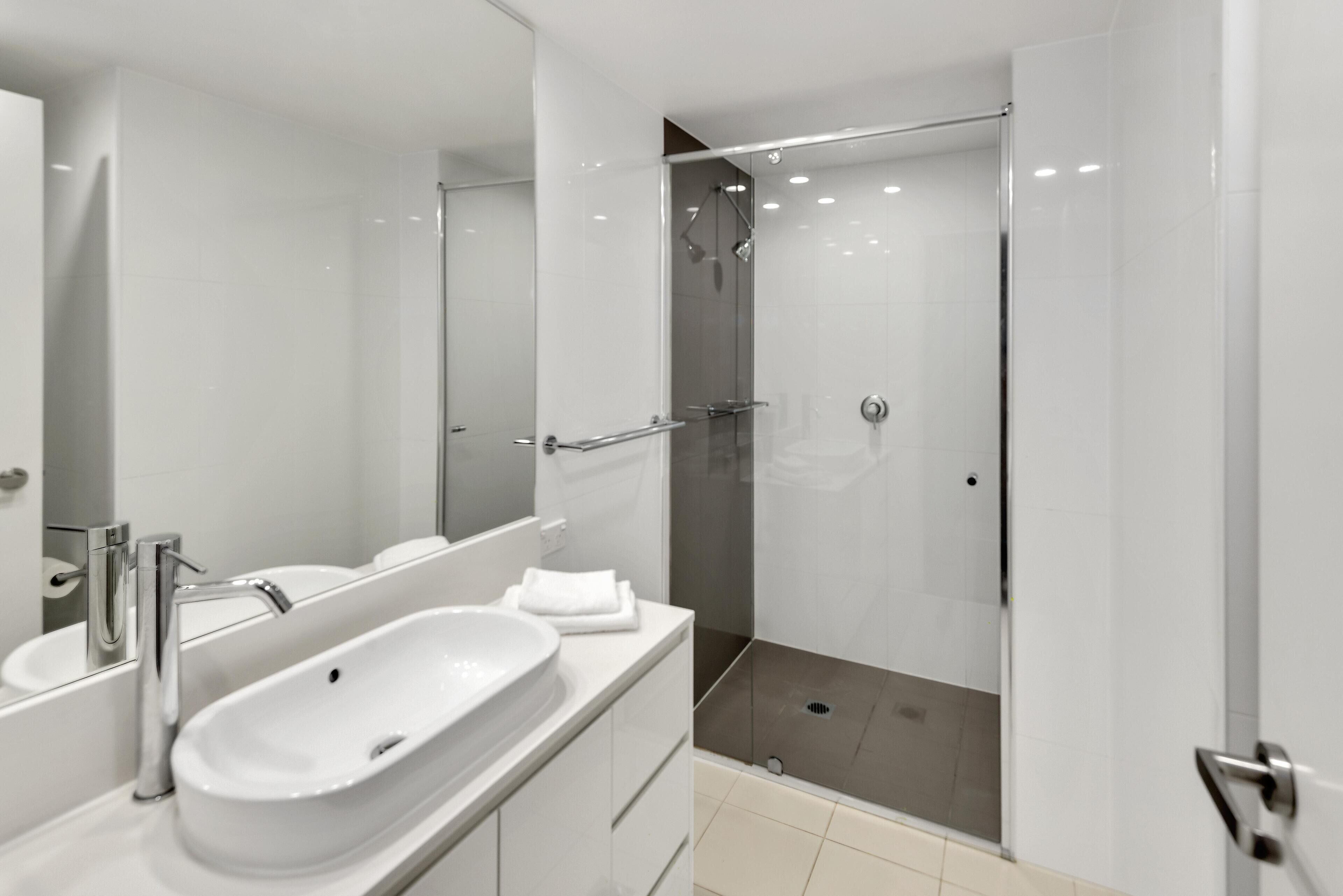 A modern bathroom with a large sink, mirror, and walk-in shower.