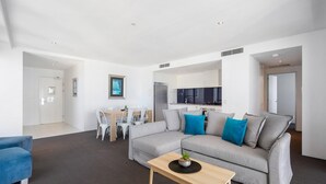 A modern living room with a grey sofa, blue cushions, a wooden coffee table, and a dining area with a white table and chairs. - Family 2 Bedroom Ocean unit at Circle on Cavill (Surfers Paradise)