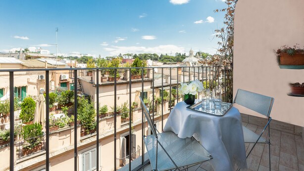 Un balcon avec une table et des chaises, donnant sur un paysage urbain avec des bâtiments et de la verdure.
