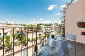 A balcony with a table and chairs, overlooking a cityscape with buildings and greenery.