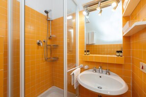 A bathroom with orange tiles, a glass shower enclosure, a sink, and a mirror.
