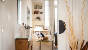 Un salon chaleureux avec un canapé blanc, une petite table ronde surmontée d’une lampe, et des étagères décoratives ornées de figurines.